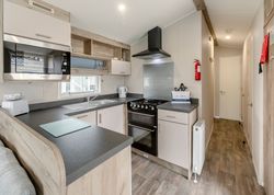 Modern compact kitchen with light wood and grey countertops, electric appliances, and a hallway leading to a door.