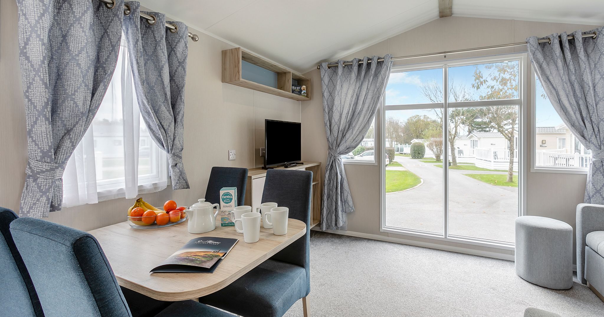 Modern mobile home interior with dining area, large windows, and living space.