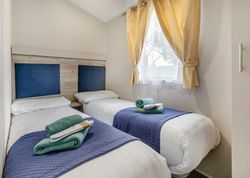 Two single beds with blue headboards, navy covers, and neatly arranged towels in a bright room with a window and yellow curtains.