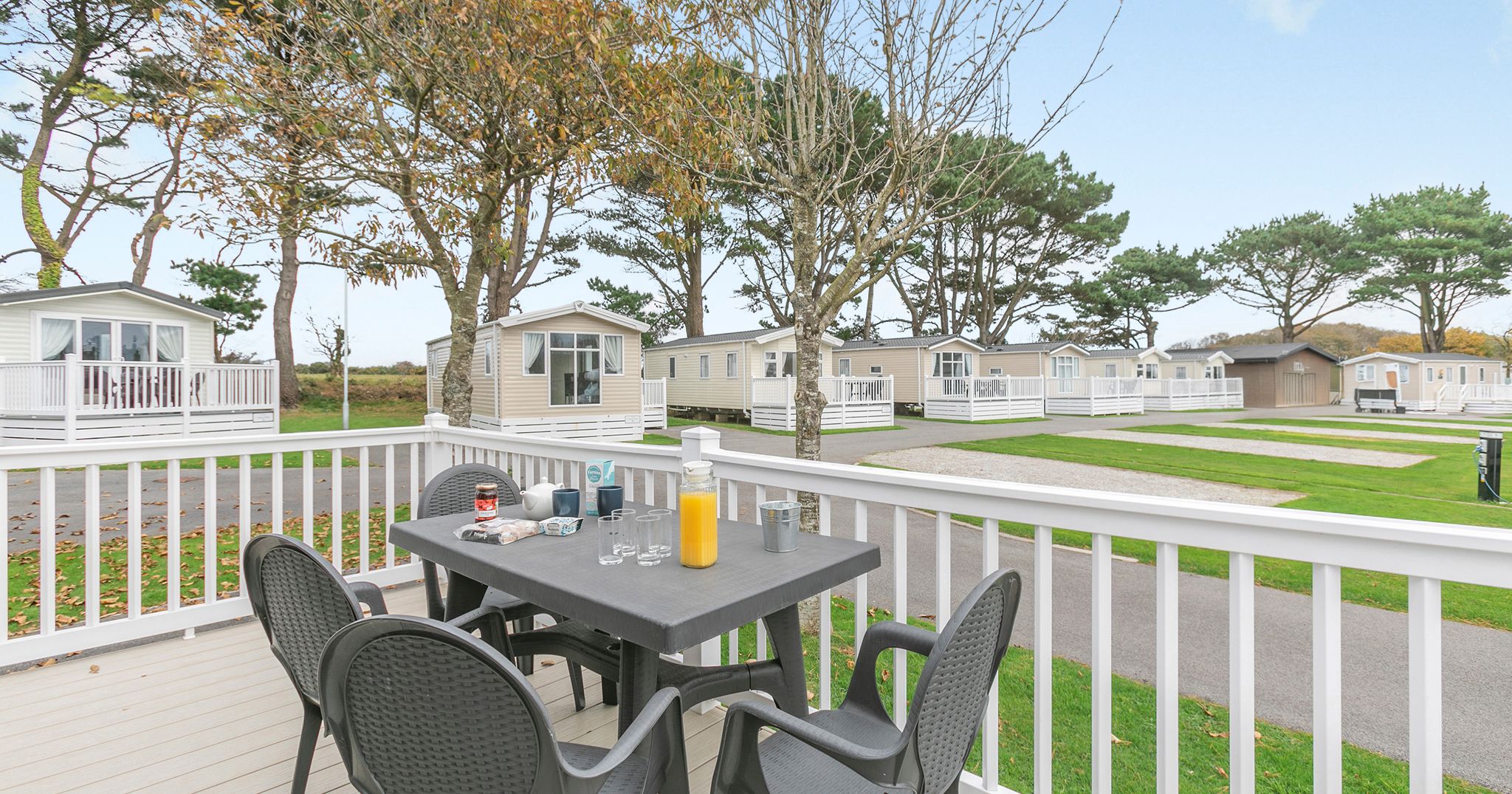 Outdoor table set on a veranda in a holiday park with mobile homes and trees in the background.