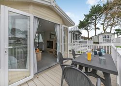 Modern mobile home with a deck featuring outdoor seating and a table set for breakfast, surrounded by similar units and trees.