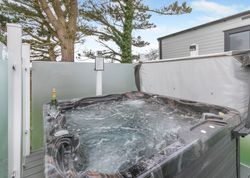 Outdoor hot tub with bubbling water beside a privacy screen and trees, with champagne and glasses on the edge.