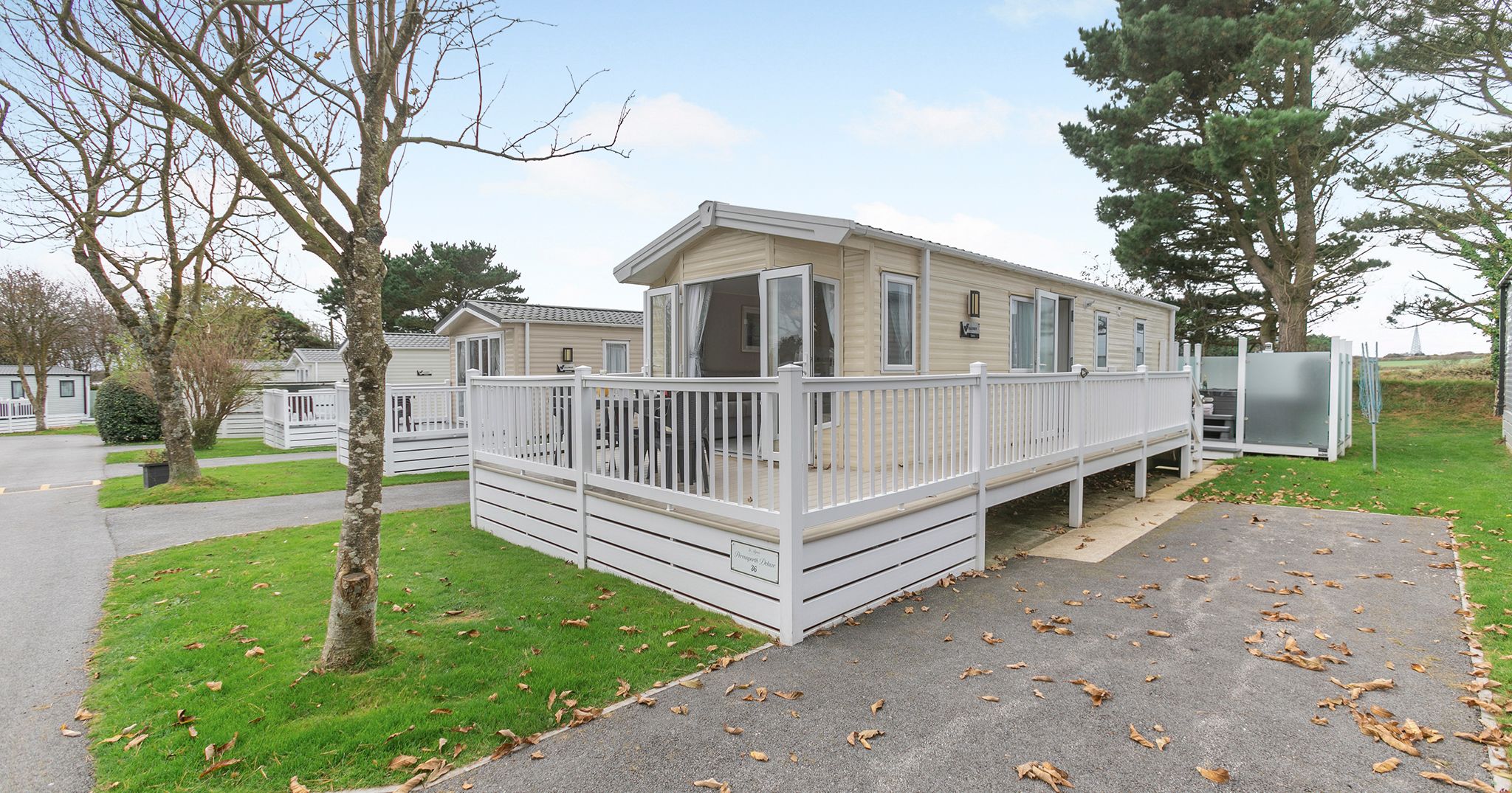 Modern mobile home with a deck and white railing in a holiday park setting.