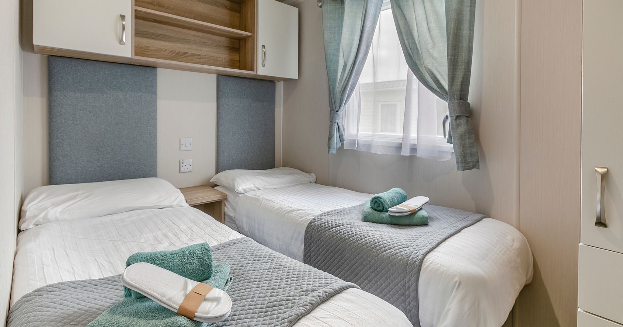 Modern twin bedroom with two single beds, folded towels, and calming decor.