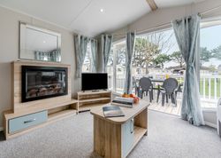 Modern living room with fireplace, TV, coffee table and large windows overlooking a patio with outdoor seating.
