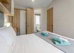 Neatly made bed with folded towels in a modern hotel room with light wood finishes.