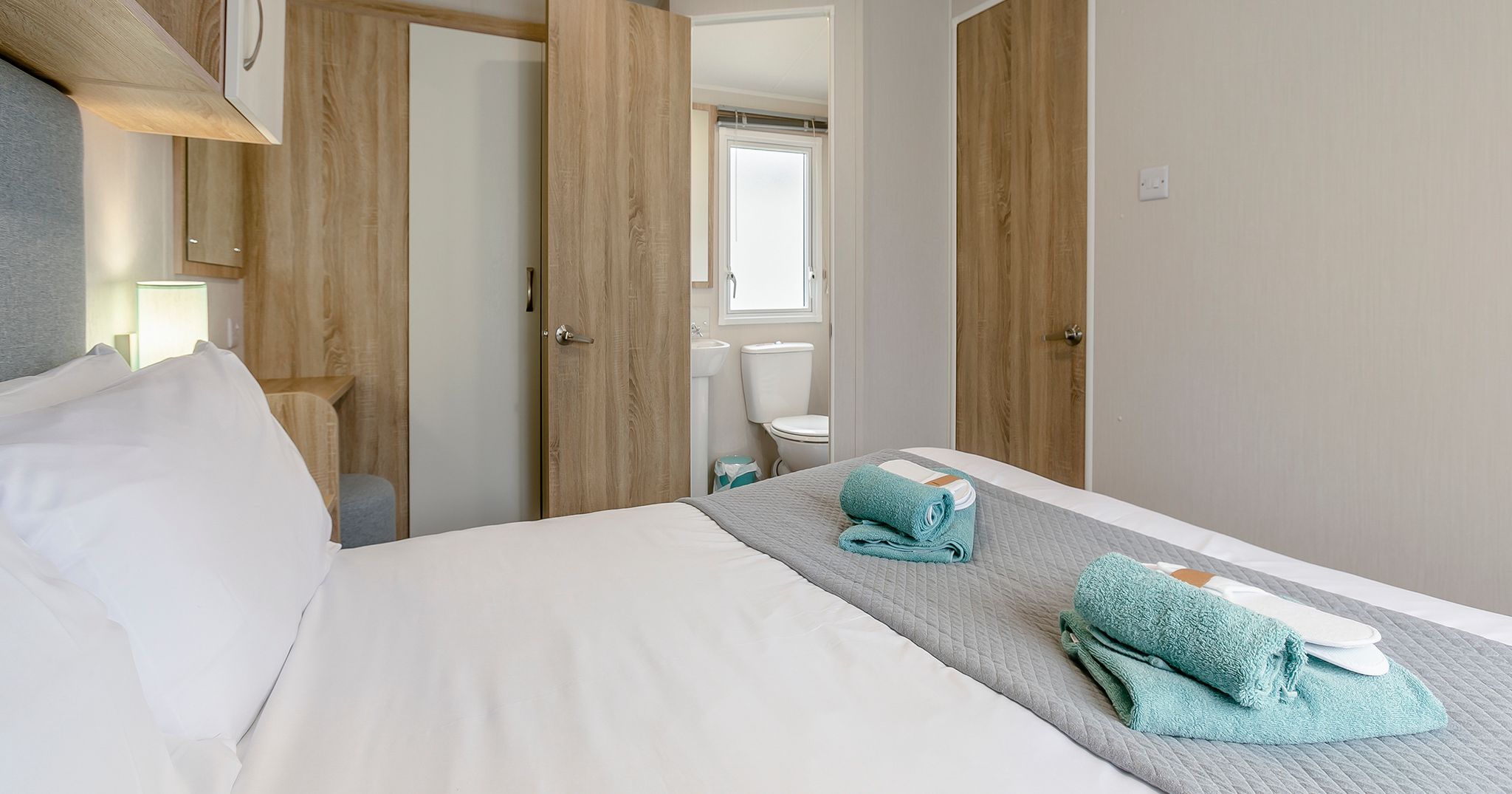 Neatly made bed with folded towels in a modern hotel room with light wood finishes.