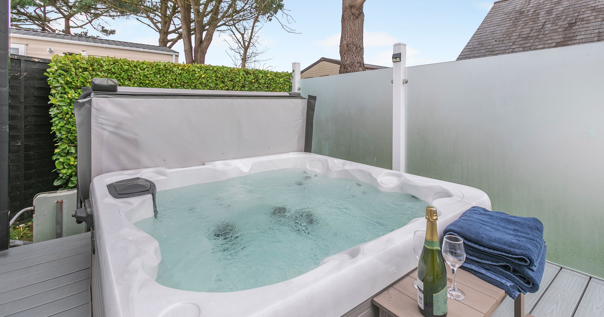 Outdoor hot tub with bubbling water, champagne, glasses, and towels on a table nearby