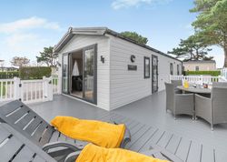 Modern mobile home with a spacious gray deck, outdoor seating, and lounge chairs with yellow blankets.