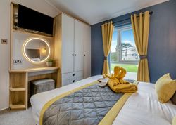Modern bedroom with yellow and gray decor, a bed, vanity, wardrobe, and window with yellow curtains.