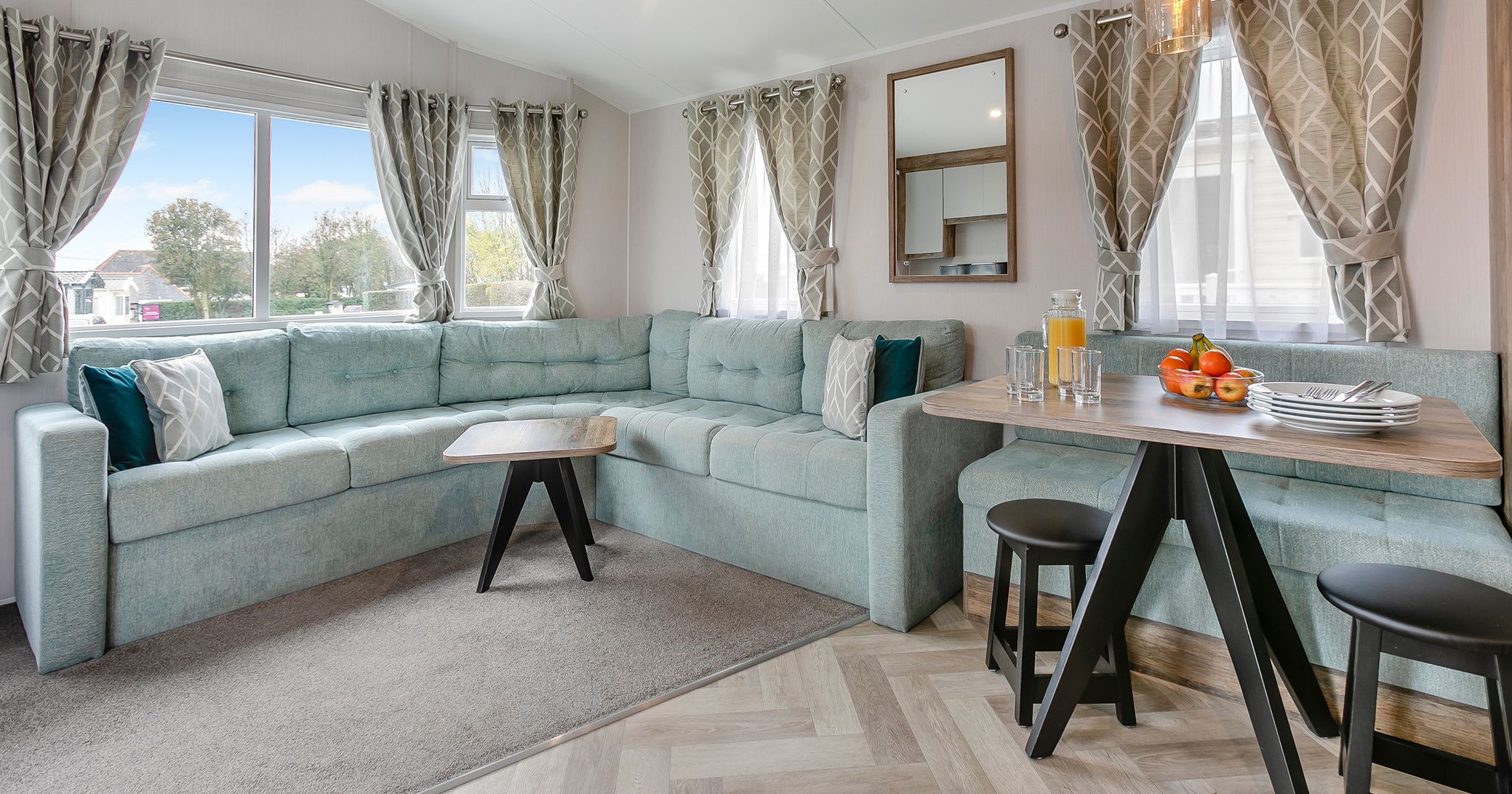 Modern living and dining area with light blue sectional sofa, wood table, and large windows with patterned curtains