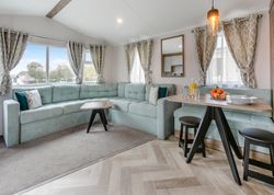 Modern living and dining area with light blue sectional sofa, wood table, and large windows with patterned curtains