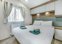 Modern bedroom with a large bed, two sets of folded green towels, and soft natural light coming through a window with curtains.