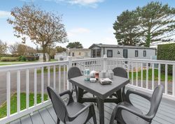 Deck with outdoor dining table and chairs in front of mobile homes at a holiday park.