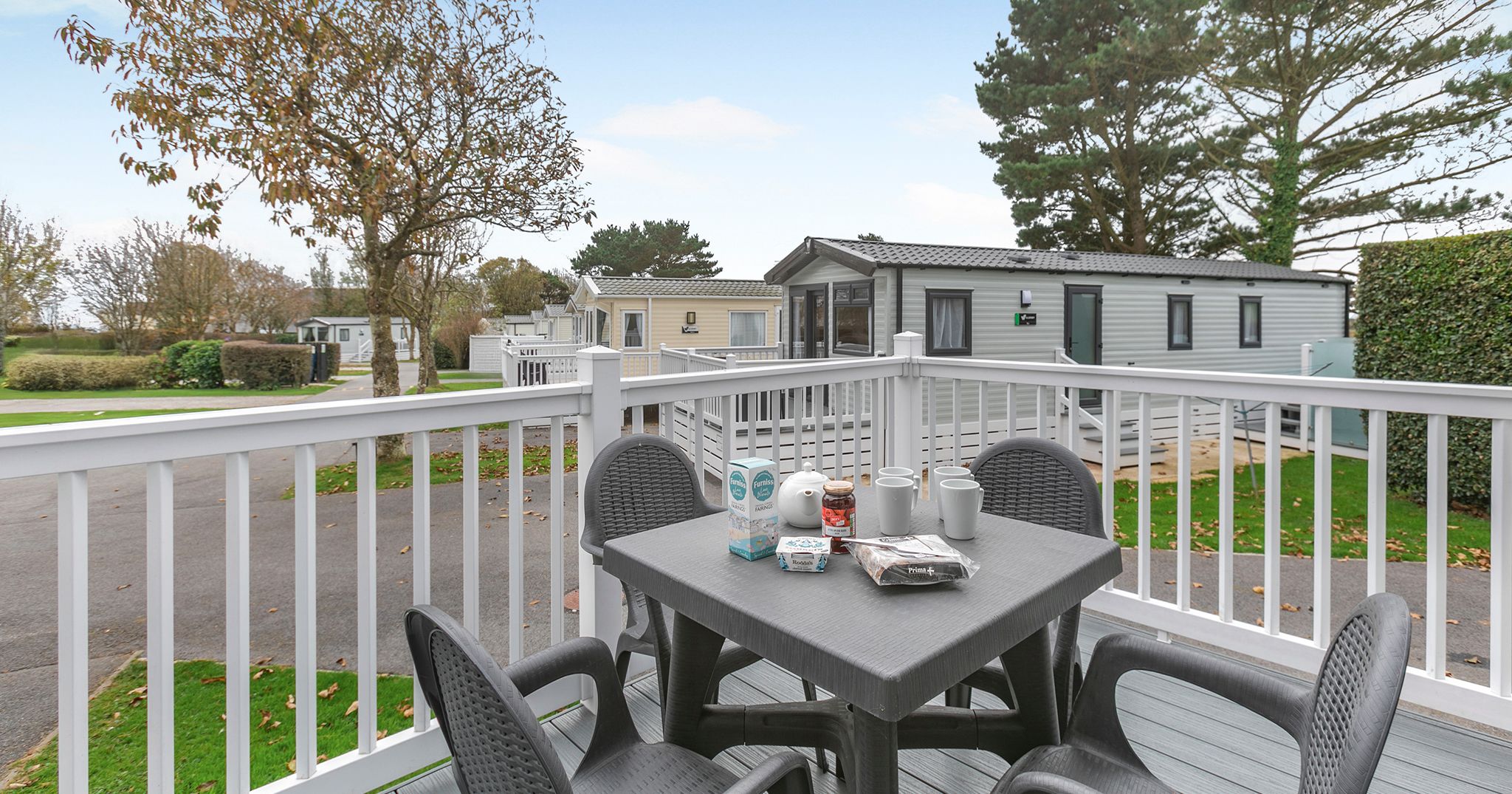 Deck with outdoor dining table and chairs in front of mobile homes at a holiday park.