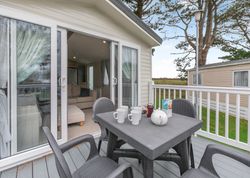 Outdoor patio area with table and chairs next to a sliding glass door leading to a cozy living room inside a modern mobile home.