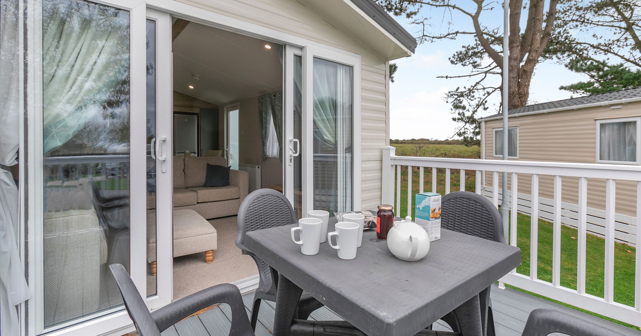 Outdoor patio area with table and chairs next to a sliding glass door leading to a cozy living room inside a modern mobile home.