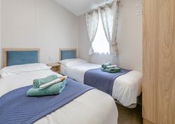 Two single beds with blue headboards and folded towels in a bright room with a window and patterned curtains.
