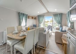 Modern living and dining area inside a caravan with large windows and patio doors opening to an outdoor deck.