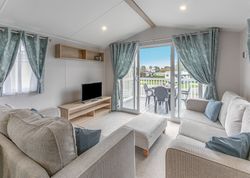Modern living room with light-colored sofas, TV, and sliding glass doors opening to a deck with patio furniture.