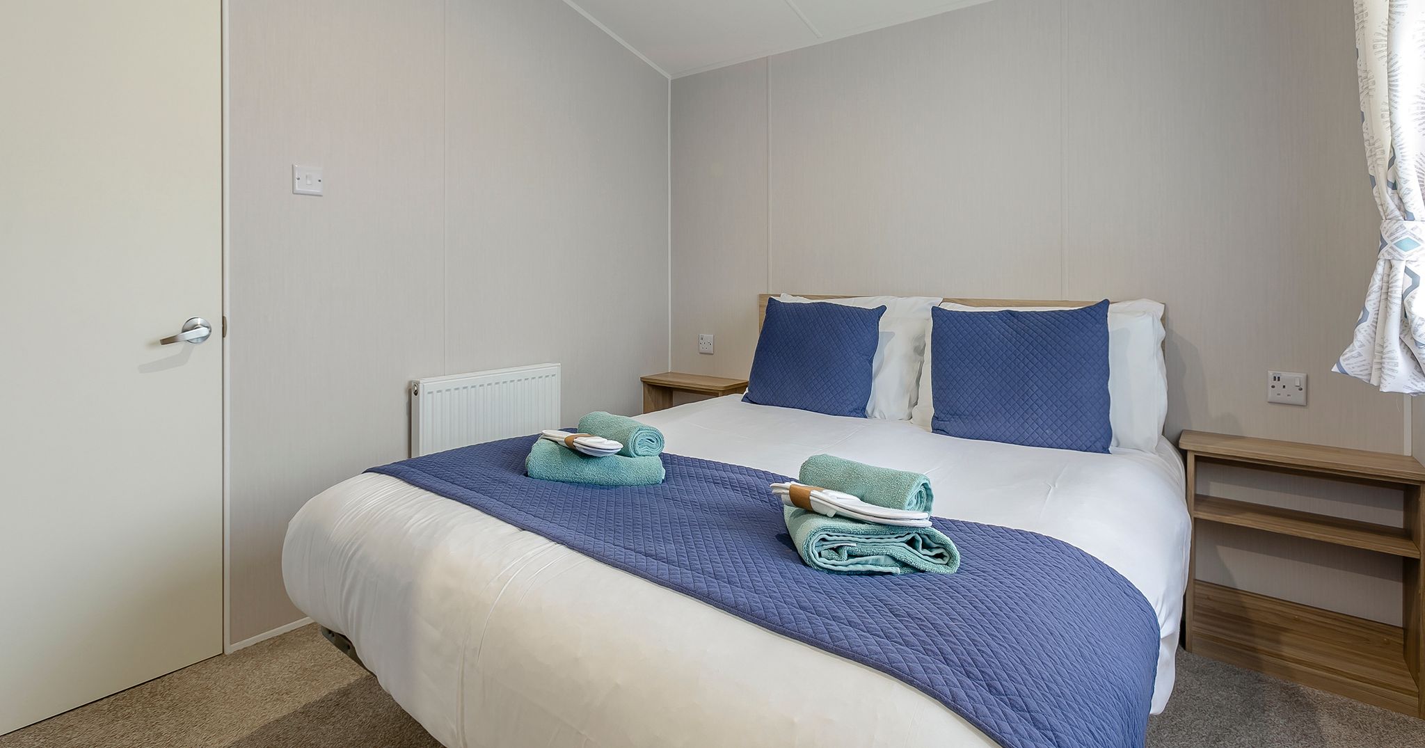 A neatly made double bed with blue pillows and blanket in a simple, modern bedroom.