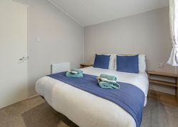 A neatly made double bed with blue pillows and blanket in a simple, modern bedroom.