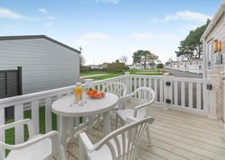 Outdoor patio area with white plastic chairs and table, fruit bowl and orange juice on table, and view of mobile homes.