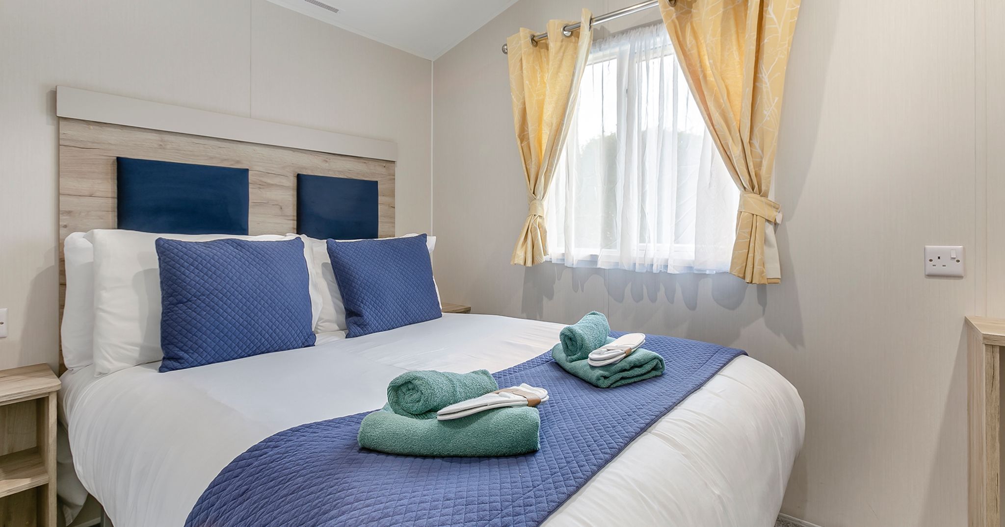 Modern bedroom with neatly made bed, blue pillows, and yellow curtains