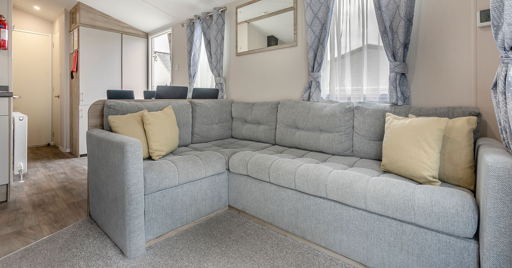 Modern living room with a large grey sectional sofa, yellow cushions, and natural light from windows with patterned curtains.