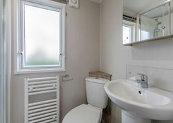 Small modern bathroom with a white toilet, sink, heated towel rail, and frosted window.