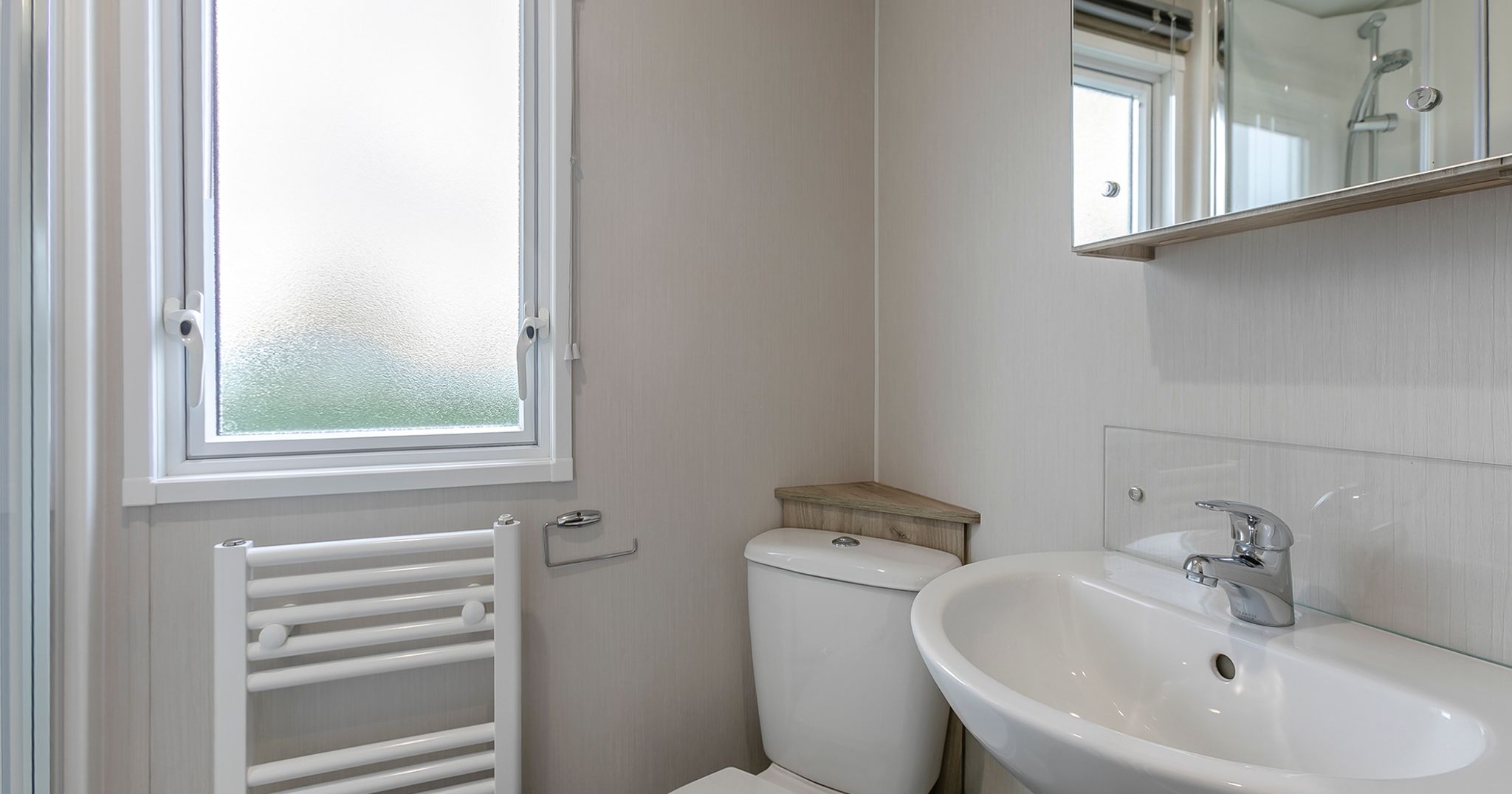 Small modern bathroom with a white toilet, sink, heated towel rail, and frosted window.