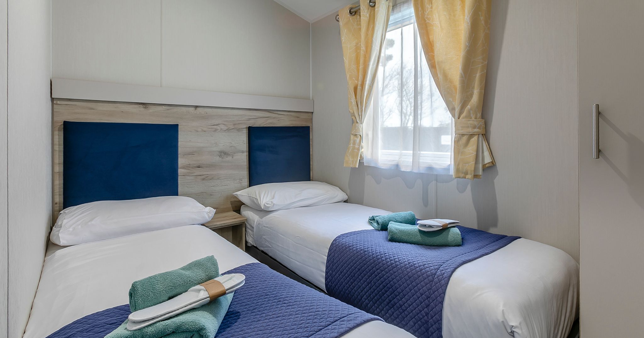 Twin bedroom with two single beds, blue headboards, and yellow curtains