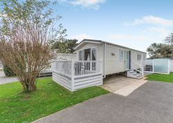 Modern mobile home with a white railing deck and steps, surrounded by greenery.