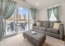 Modern living room with grey sofa, ottoman, and sliding glass doors leading to a patio with outdoor chairs and a table.