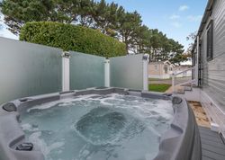Outdoor hot tub next to a static caravan with privacy glass panels and trees in the background