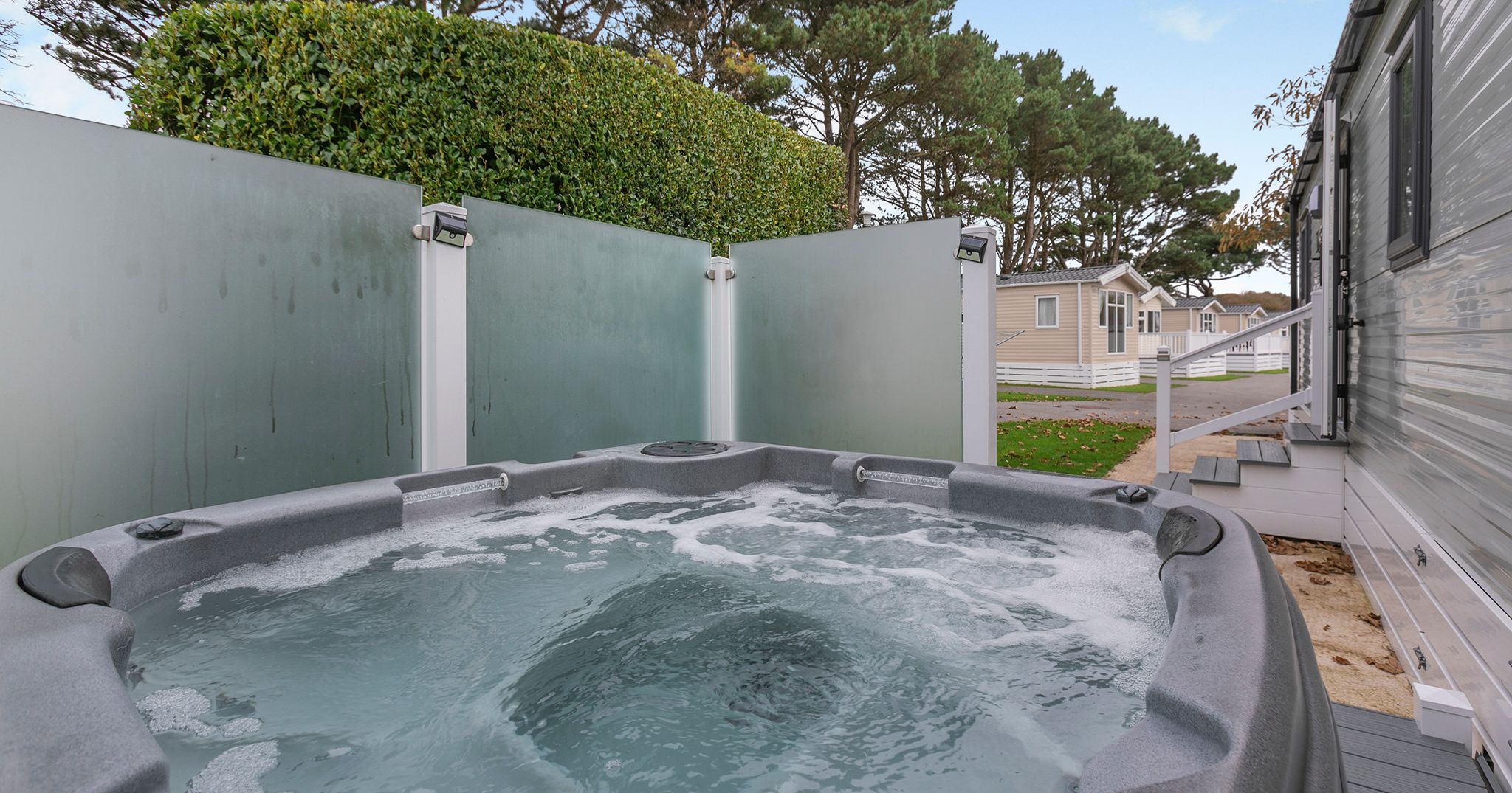 Outdoor hot tub next to a static caravan with privacy glass panels and trees in the background