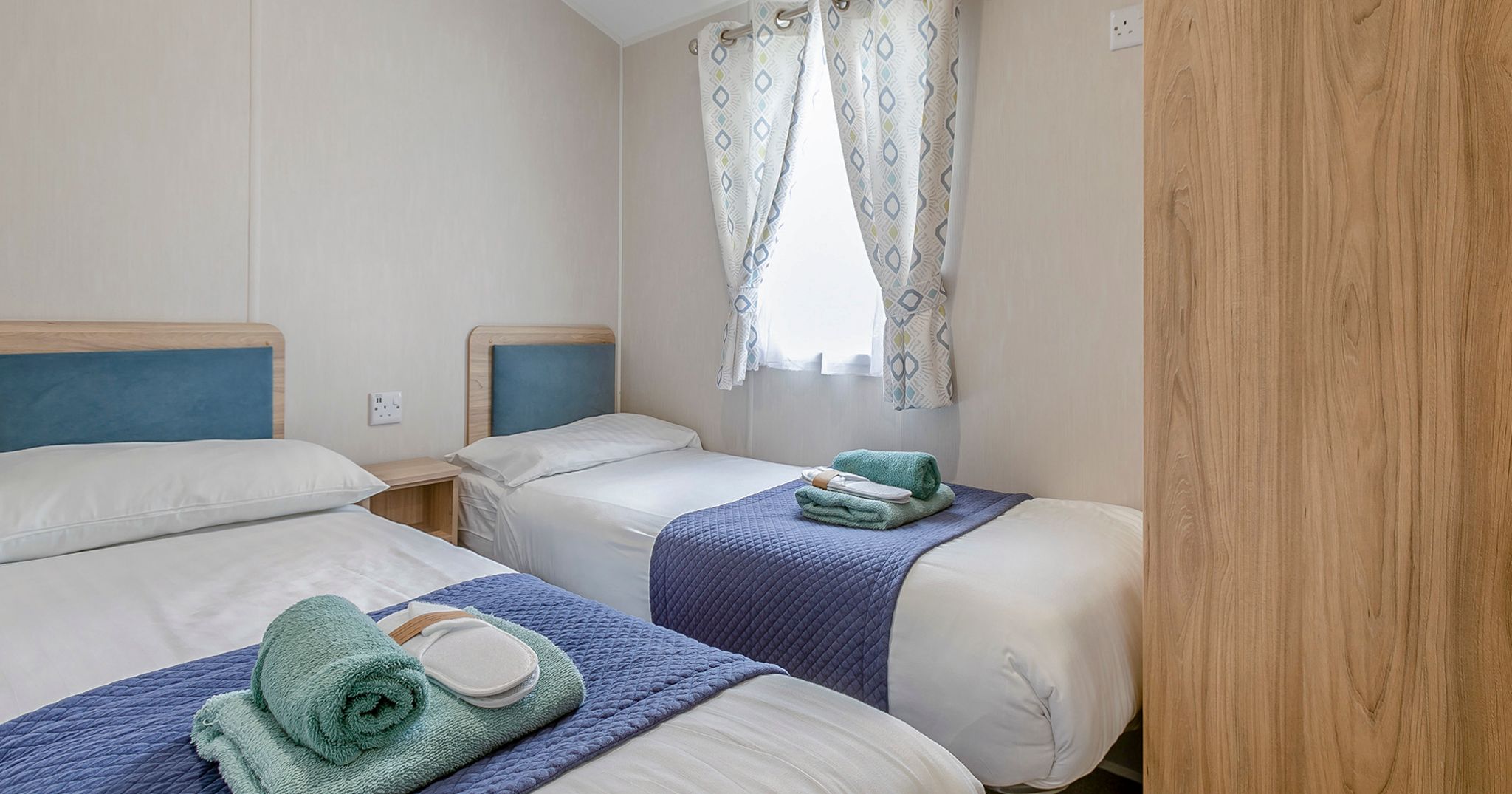 Twin bedroom with two single beds, blue headboards, and folded towels on each bed.
