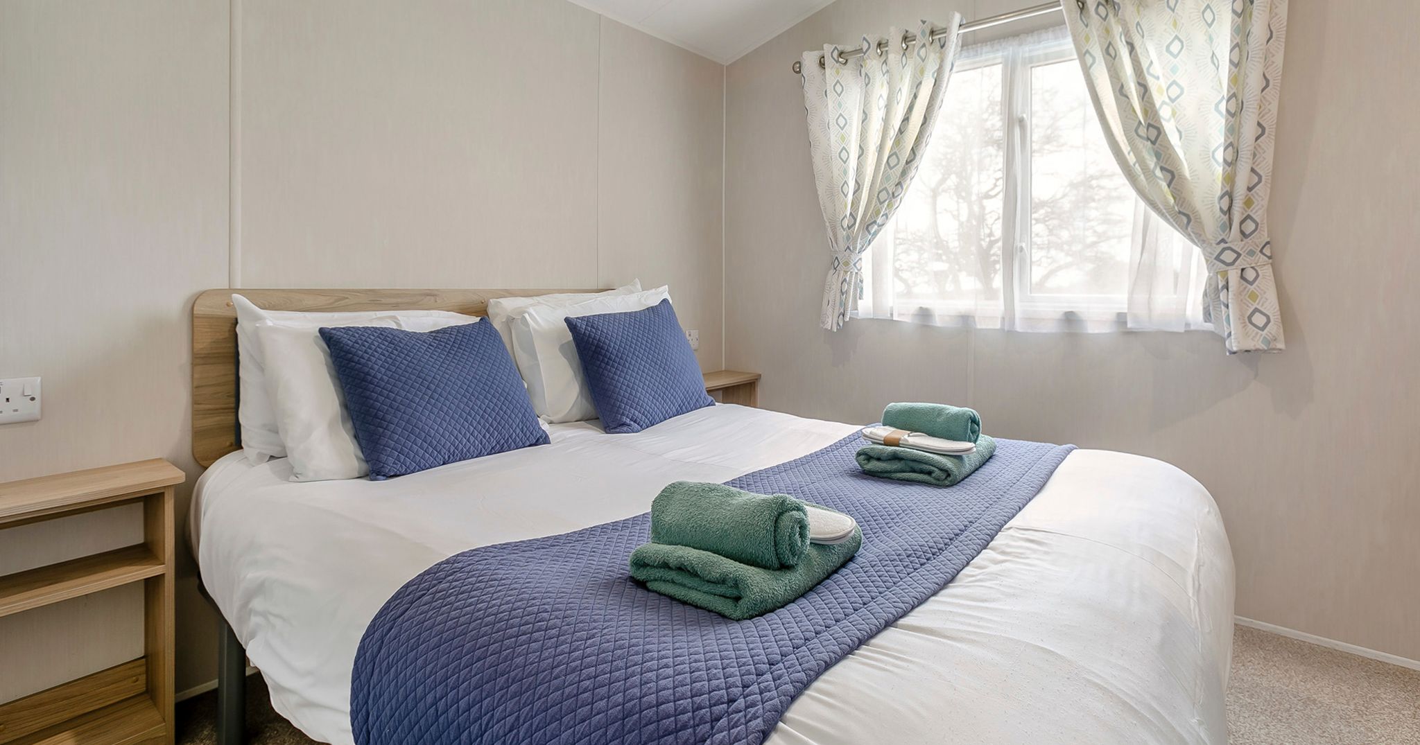 A neatly made bed in a bright bedroom with blue accents and folded towels