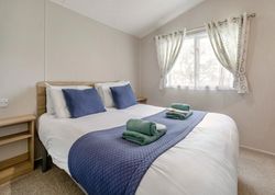 A neatly made bed in a bright bedroom with blue accents and folded towels