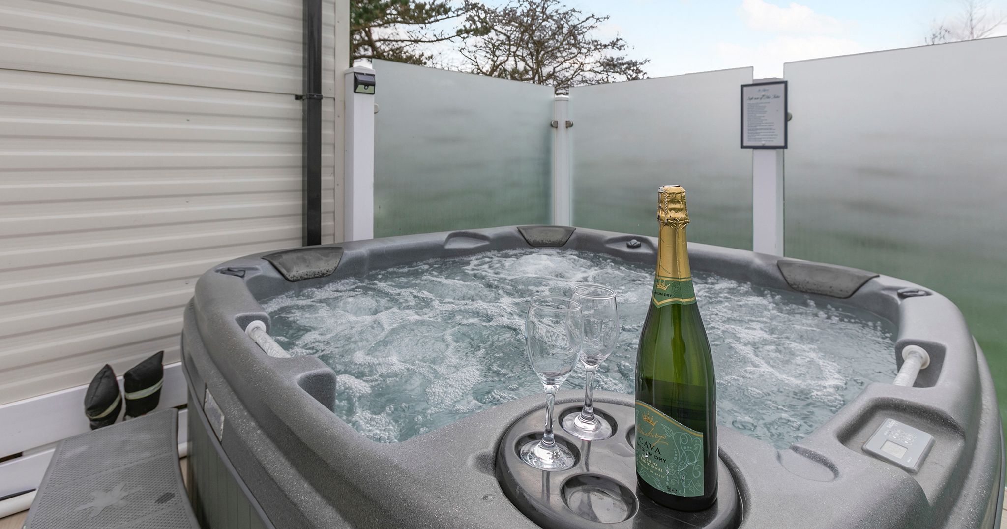 Outdoor hot tub with a bottle of sparkling wine and two glasses on the edge
