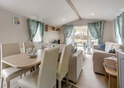Modern living and dining area inside a holiday caravan with neutral furnishings and large windows overlooking a deck.