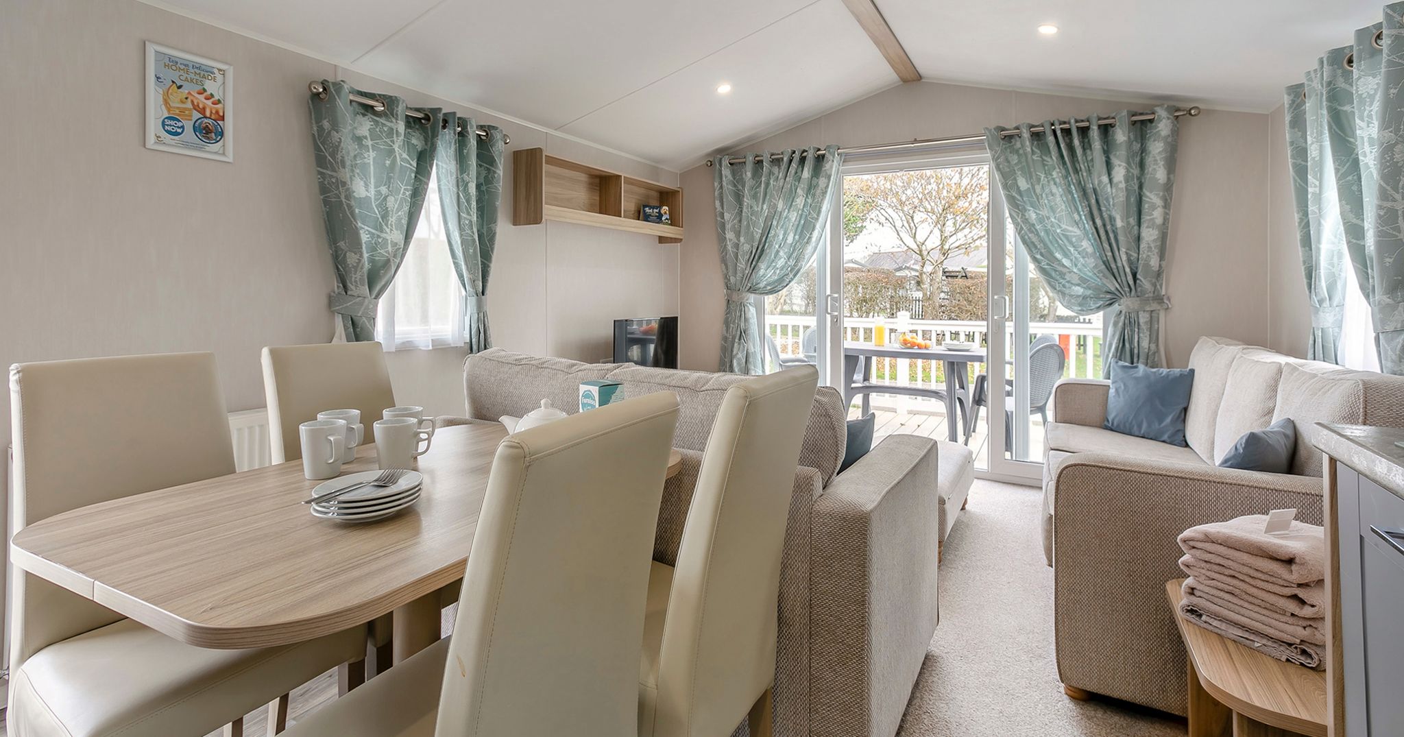 Modern living and dining area inside a holiday caravan with neutral furnishings and large windows overlooking a deck.