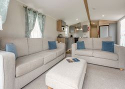 Modern living room with beige sofas, blue pillows, and a view into the kitchen.