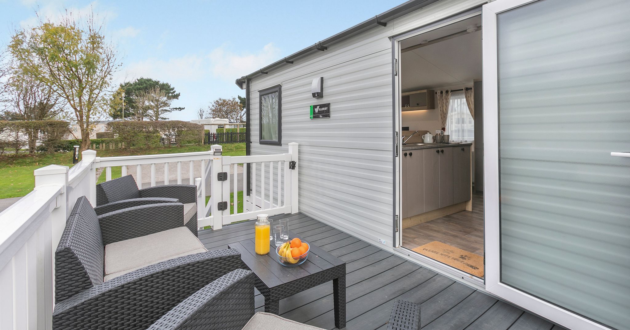 Outdoor seating area on the deck of a modern mobile home with open door to kitchen
