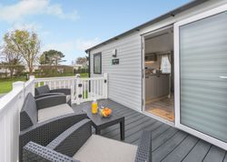 Outdoor seating area on the deck of a modern mobile home with open door to kitchen