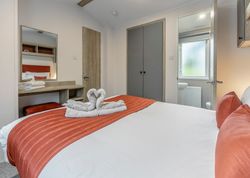 Modern bedroom with orange accents, heart-shaped towel art on the bed, and an en-suite bathroom