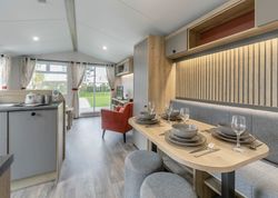 Modern open-plan living and dining area with kitchen, table set, sofa, and large windows.