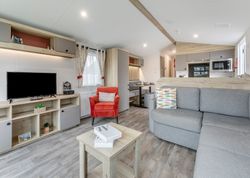 Modern open-plan living area with grey corner sofa, orange armchair, TV unit, and kitchen
