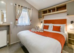 Modern bedroom with orange accents, a double bed, and decorative towel swans