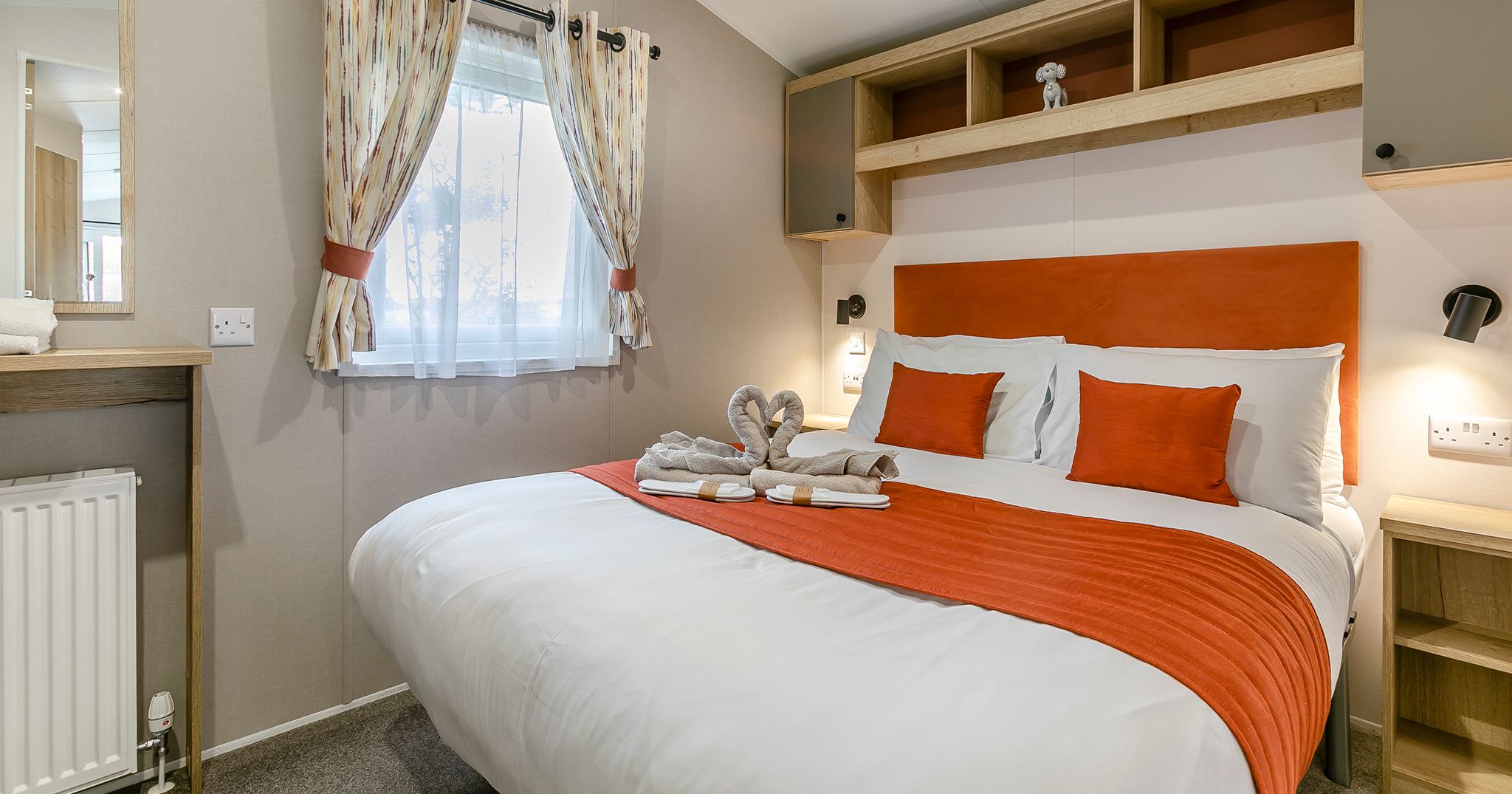 Modern bedroom with orange accents, a double bed, and decorative towel swans